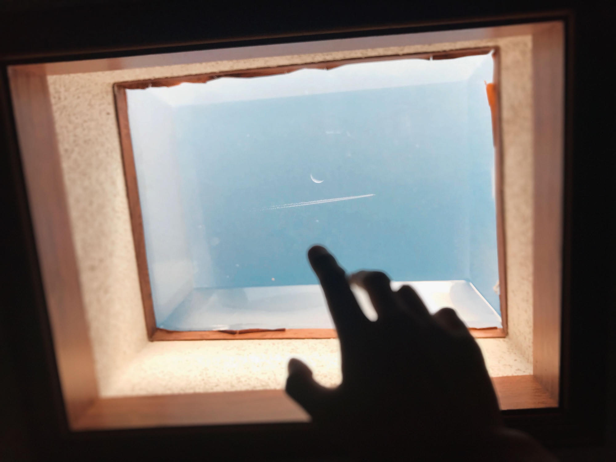 A hand pointing at a crescent moon through a small window