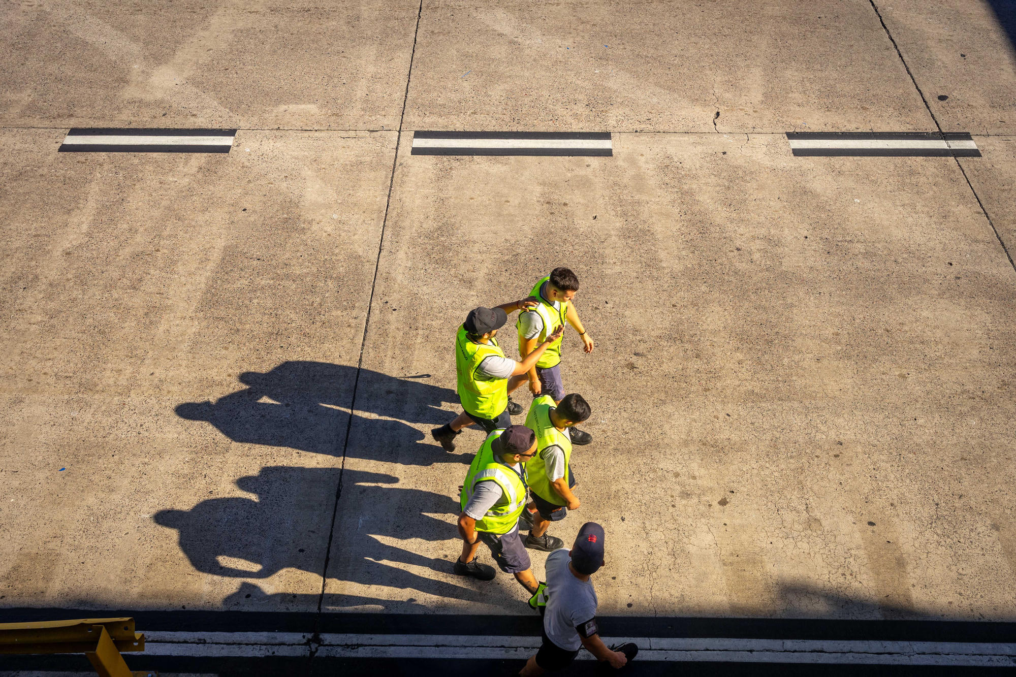 Site crew in high-visibility vests crossing a concrete apron, seen from above