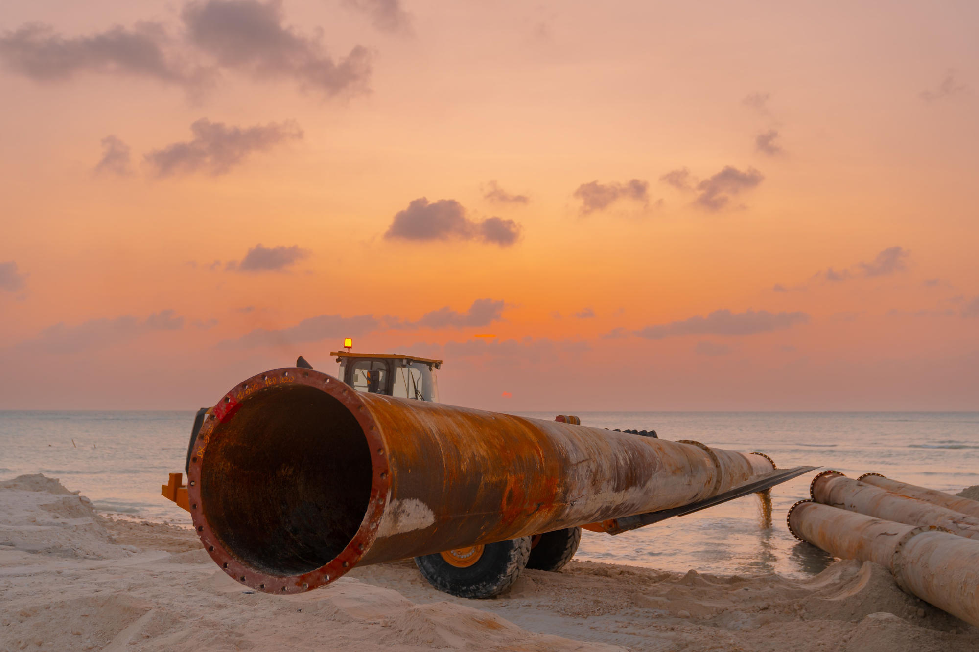 Large diameter pipeline being laid on a shoreline at sunset