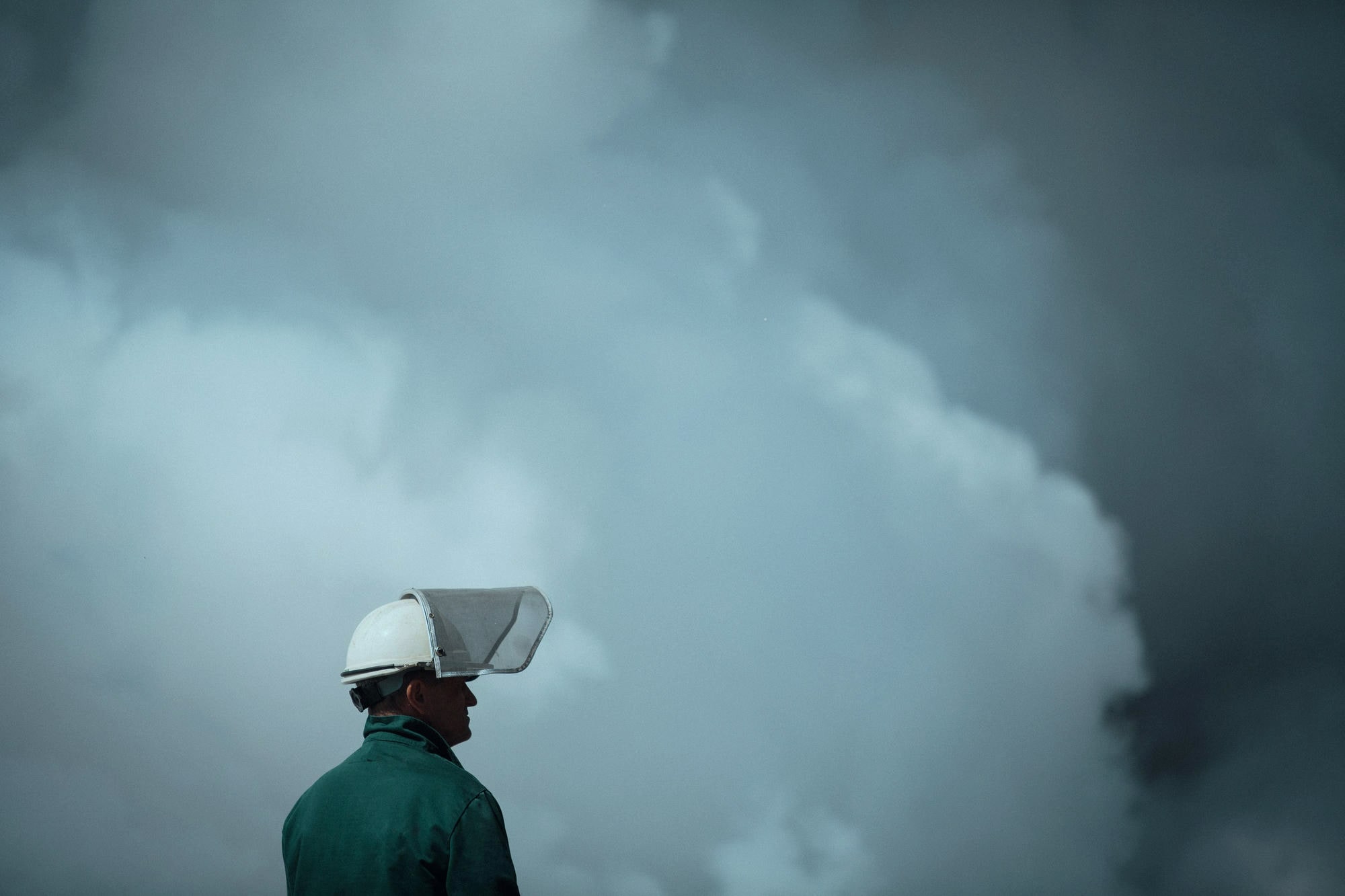 Plant operator in a hard hat standing against a plume of steam