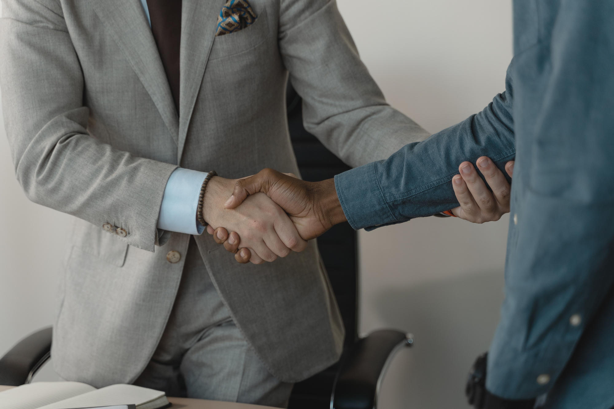 Two people shaking hands across a desk after closing a deal