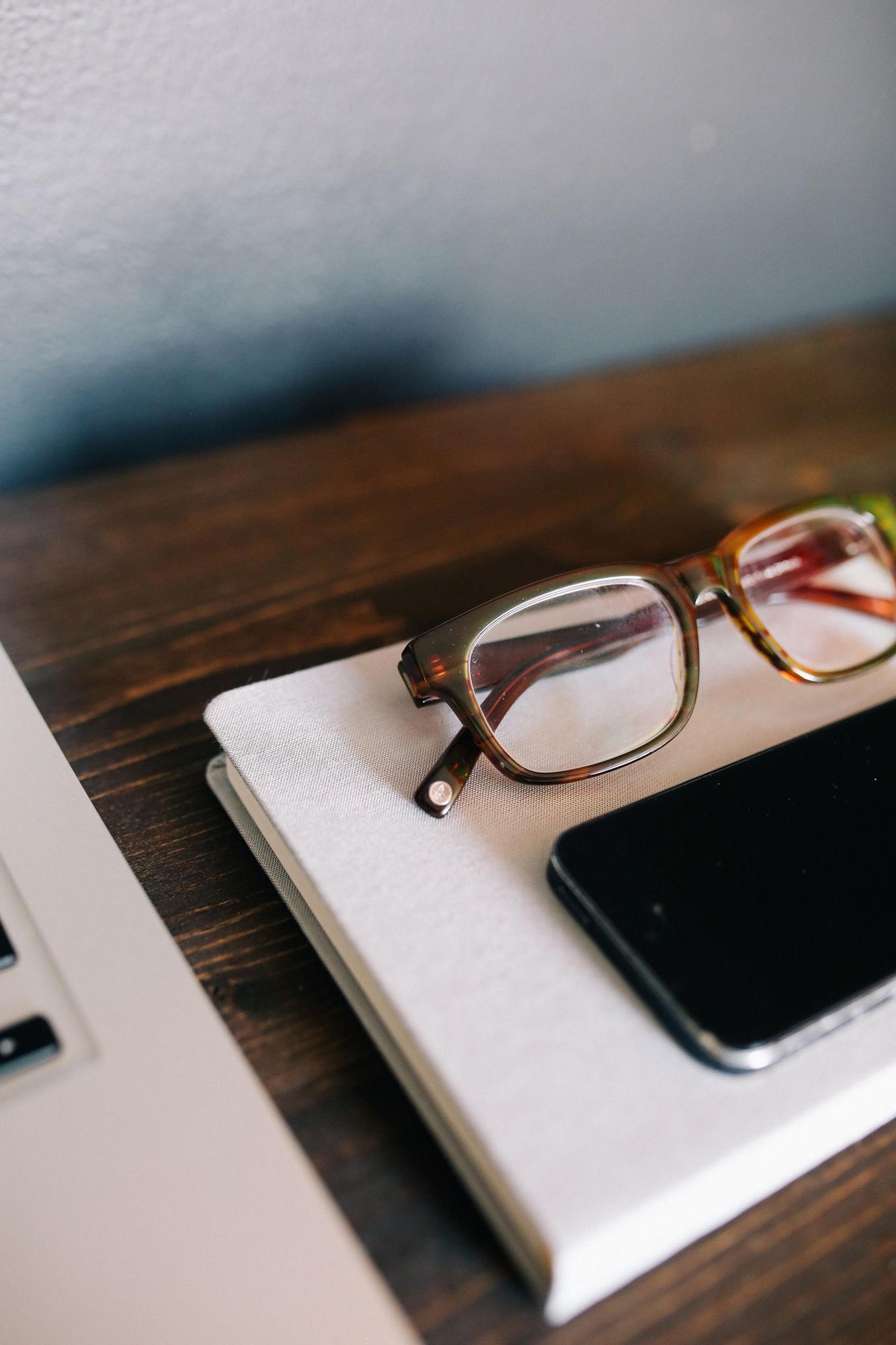 Reading glasses resting on a closed notebook beside a laptop